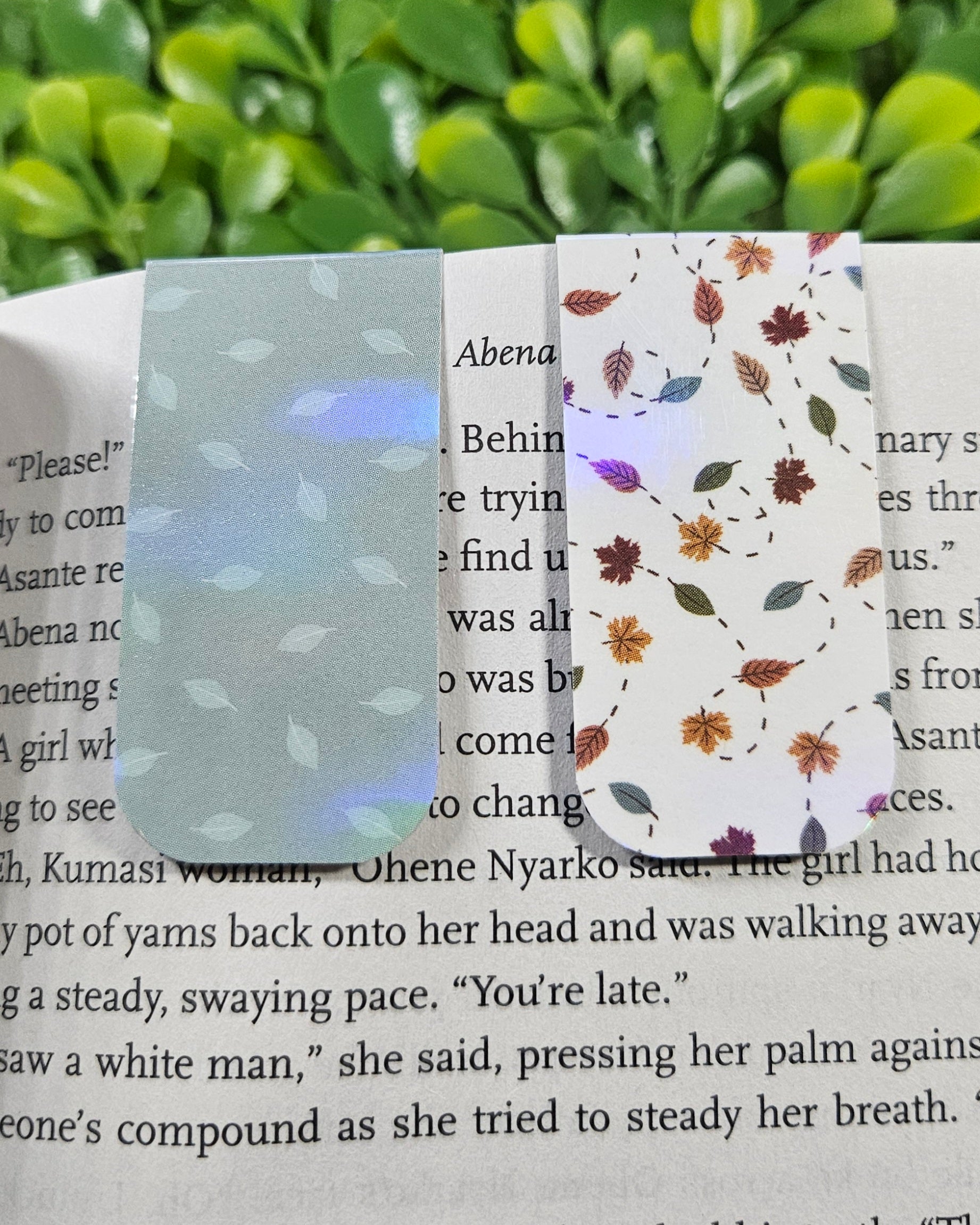 Handmade holographic magnetic bookmarks with leafy designs on a book
