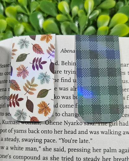 Handmade holographic magnetic bookmarks with a leafy and plaid designs on a book